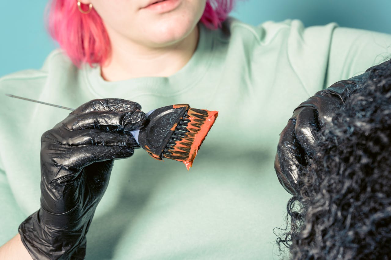 services-img Close-up of a hairstylist dyeing curly hair in a salon environment.