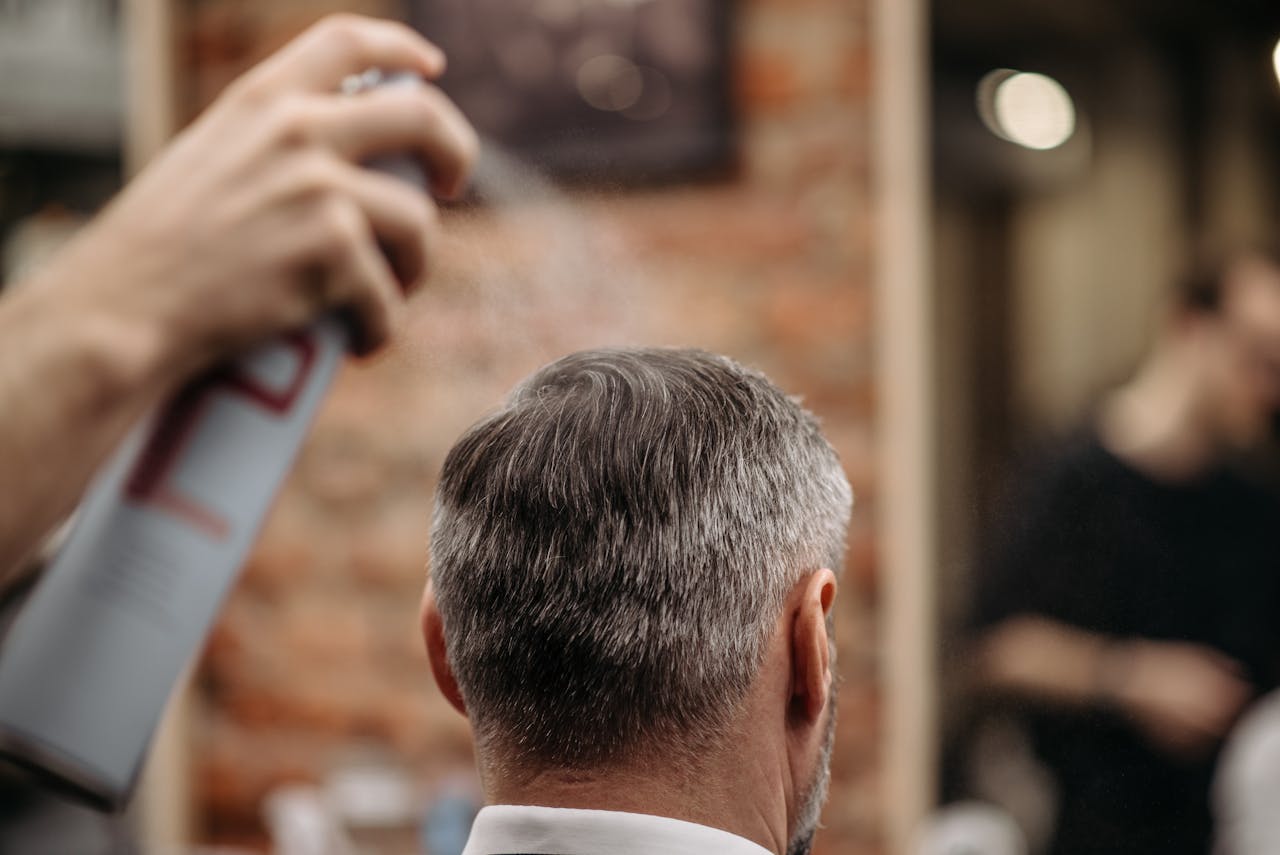 A professional barber styles a man's hair with hairspray in an urban barbershop.