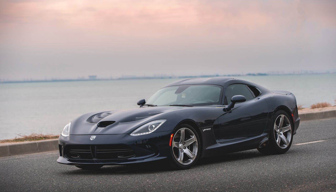 Luxurious black sports car parked on a coastal road under a serene sky.